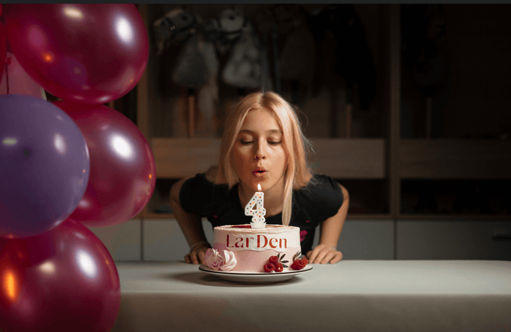 Lara blowing out a number four candle on a LarDen birthday cake beside colourful balloons