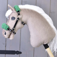 A Hobby Horse LarDen toy features a beige plush head, white yarn mane, and a black halter with green fur (leatherette). It stands against a wooden gray background.