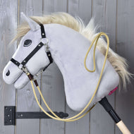 The Hobby Horse LarDen Western Reins Dakota, a gray hobby horse with a blonde mane, black bridle, and yellow rope with snap hooks, hangs on a wooden wall in a black holder—perfect for training sessions.