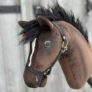 A close-up of the Hobby Horse LarDen "Hobby Horse Lucas with Black Halter" (size S), featuring a brown coat, black mane, white facial stripe, painted teardrop, and bridle, set against a blurred wooden background.