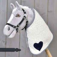 The Hobby Horse LarDen "Blanket cube blue" is a plush hobby horse with a gray face, black bridle, and a blue-accented blanket, mounted on a wooden stick and set against a wooden background.