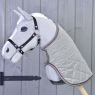 A gray plush hobby horse by Hobby Horse LarDen with a black bridle and the Blanket Silver Eleganza stands against a wooden wall with vertical panels.