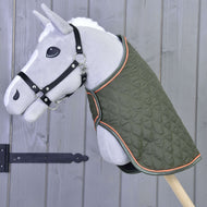 A gray plush hobby horse on a stick, featuring the Hobby Horse LarDen Blanket Sport in green with orange trim and a black halter, stands before a wooden wall with a black iron hinge.