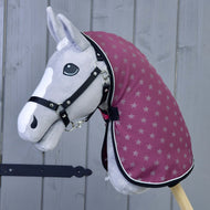 A gray hobby horse by Hobby Horse LarDen, wearing a black bridle, maroon star-patterned hood, and the Stable Blanket Purple, stands against a wooden gray background. It features a white blaze and black button eyes.