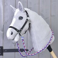 The Hobby Horse LarDen Reins Flag CZ is a gray plush hobby horse with a white mane, black bridle, handmade reins, and a blue-red-white braided polypropylene rope lead, mounted on a wooden stick against a gray wood background.