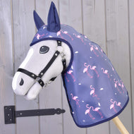 A Hobby Horse LarDen Raincoat Flamingo, a grey hobby horse in a navy blue raincoat hood with pink flamingos, is placed before a wooden wall featuring a black metal hinge.