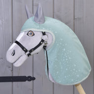 The Hobby Horse LarDen "Raincoat Greeny" plush horse, dressed in a green raincoat with water droplet patterns and a black bridle, stands by a gray wooden wall. Embroidered details and upright ears offer fun all-weather play.