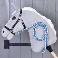 The Hobby Horse LarDen "Hobby Horse - Knitted Lead Rope Double Blue" features a gray plush horse with a black bridle and a hand-knitted blue lead rope with a premium carabiner, displayed against a wooden wall.
