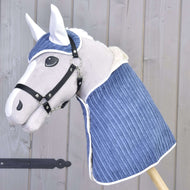 The Hobby Horse LarDen Set Manchester Plum features a plush hobby horse with a white face, black bridle, and blue quilted covering, plus a matching ear bonnet, posed against a light wooden wall.