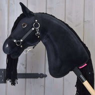 The Hobby Horse LarDen's Hobby Horse Maximus with Black Halter features shiny button eyes and a yarn mane, mounted on a wooden stick, displayed in front of a light wooden plank wall.