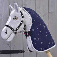 A gray plush hobby horse by Hobby Horse LarDen features a black bridle and the Stable Blanket Night Sky, mounted on a wooden stick against a light wooden wall background.