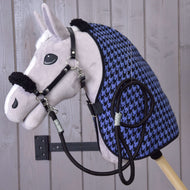 A Hobby Horse LarDen Set Harmony Blue plush hobby horse with black halter, reins, and a blue-black houndstooth stable blanket is mounted on a wall against a light wood plank background.