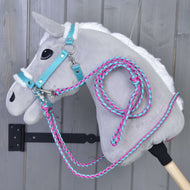 The Set Perfect Combination Turquoise by Hobby Horse LarDen, a plush gray hobby horse with a white mane, turquoise bridle, fur-padded halter, and pink-and-blue rope reins, hangs against a gray wooden wall.