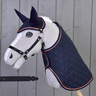 The Hobby Horse LarDen "Set Winner" features a stuffed horse head on a stick, dressed in a quilted navy blanket and matching ear bonnet with orange trim, posed against a wooden wall.