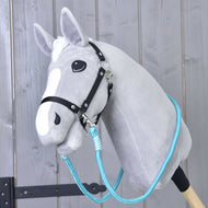 The Hobby Horse LarDen Reins Atlantis is a gray plush hobby horse with a black bridle and blue polypropylene rope reins on a wooden stick, shown in front of a rustic wooden wall.