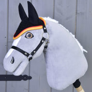 A close-up of a gray Hobby Horse LarDen with a bridle and the crocheted Flag ear bonnet for insect protection, featuring a detailed eye, white mane, black ears, and orange-trimmed bonnet, set against wood.