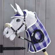 A Hobby Horse LarDen Set Cube, featuring a blanket, ear bonnet, lead rope, and fur halter, is displayed on a wooden wall near a black gate hinge. The accessories highlight the quality and charm of Hobby Horse LarDen products.