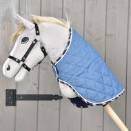 A plush hobby horse on a wooden stick wears the Hobby Horse LarDen Blanket Beautiful Jeans and a black halter, positioned against a light wooden wall for added protection.