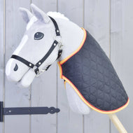 The Hobby Horse LarDen Blanket Flag, a gray hobby horse toy with a black bridle and quilted blanket with orange trim, is mounted on a wooden stick in front of a gray wooden fence.