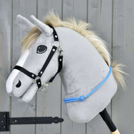 The Hobby Horse LarDen "Cordeo Sky" is a gray plush hobby horse with a white mane, black bridle, and blue rope, designed for riding with or without the bridle. It stands against a wooden background and has a friendly expression.
