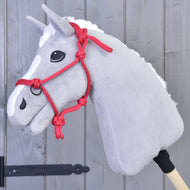 A gray Hobby Horse LarDen with a white mane, black eyes, and a vivid red rope halter (Rope halter red) is mounted on a wooden stick and positioned before a gray wooden wall.