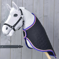 A gray hobby horse toy with a black bridle features the Hobby Horse LarDen Travel Rug Luxury—quilted black, trimmed in red, white, and blue—posed against a wooden wall background.