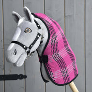 The Hobby Horse LarDen gray hobby horse, featuring a black bridle and the Stable Blanket Pink, is mounted on a wooden stick and set against a gray wooden wall.