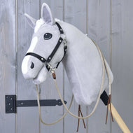 A grey plush hobby horse by Hobby Horse LarDen, featuring the Split Western Reins Dallas and a black bridle, is mounted on a wooden stick in front of a grey wooden wall.