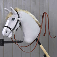 A gray stuffed hobby horse from Hobby Horse LarDen with a black bridle and Split Western Reins Dark Brown is mounted on a wooden stick, set against a gray wooden wall.