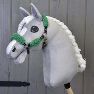 A gray plush hobby horse from Hobby Horse LarDen, featuring a black leatherette halter with full green fur, is set against a wooden panel background.