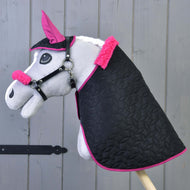 The Hobby Horse LarDen Set Thermo Pinkie includes a gray hobby horse with a pink-trimmed black blanket, matching pink ear bonnet, and halter with fur, displayed against a wooden background.