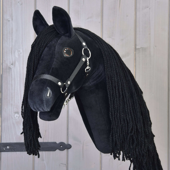 Black hobby horse with long black yarn mane and bridle, mounted on a wooden background with a dark metal hinge.