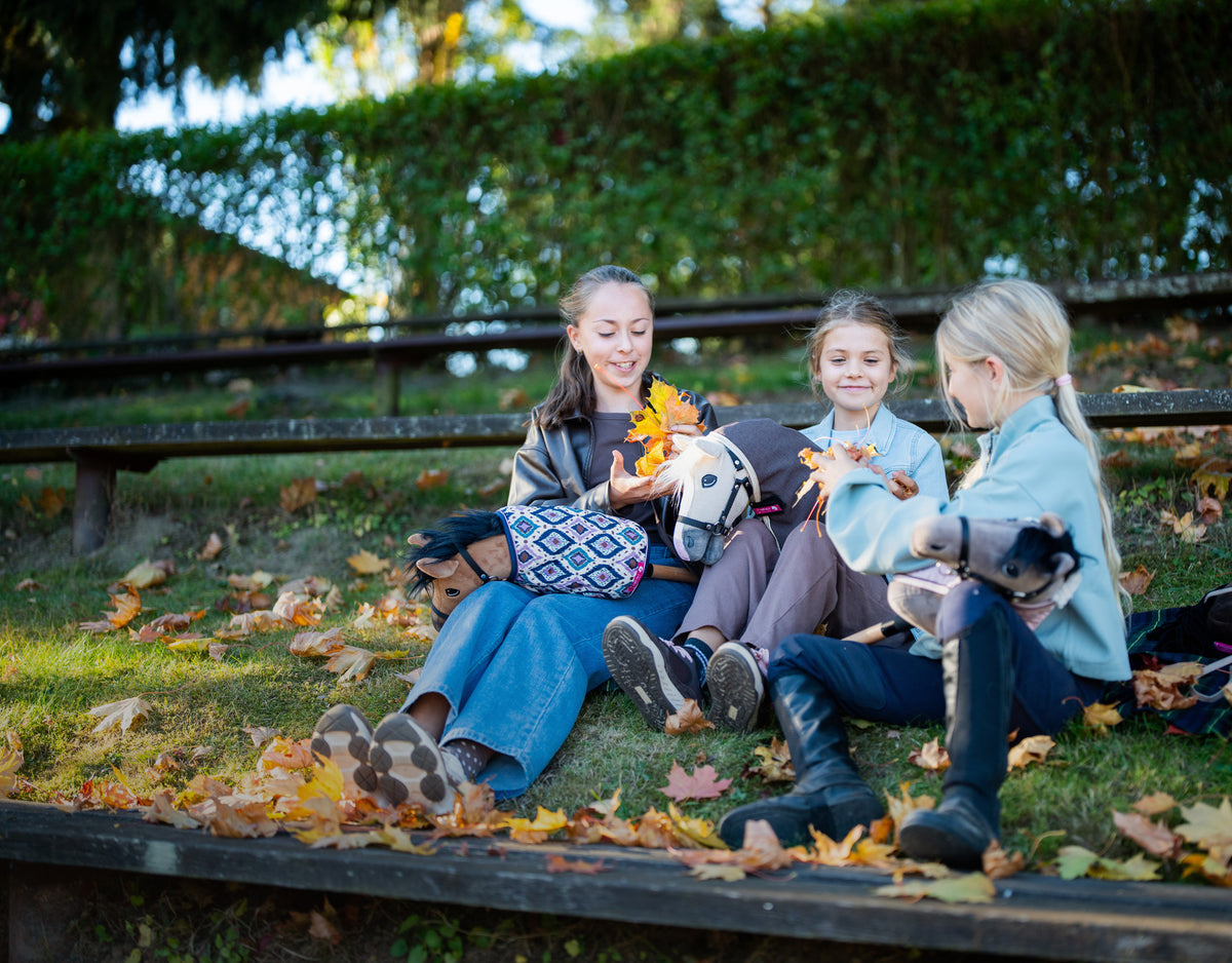 Tři dívky s Hobby Horse na podzimních schodech plných listí