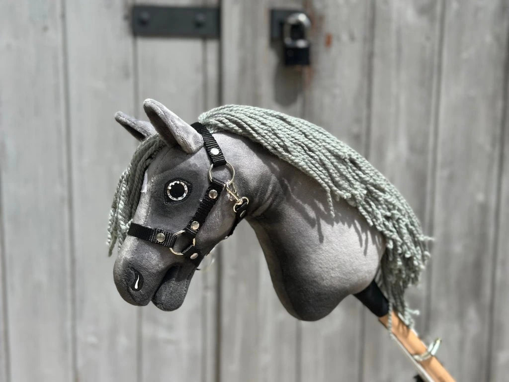 The Hobby Horse LarDen "Little Prince" (size XS), a gray Hanoverian stallion with a black halter and long gray yarn mane, is shown in front of a weathered wooden door.