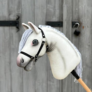 The Hobby Horse Atlas with Black Halter by Hobby Horse LarDen, featuring a white Appaloosa design and gray yarn mane, stands before a wooden door secured with a metal latch and padlock.