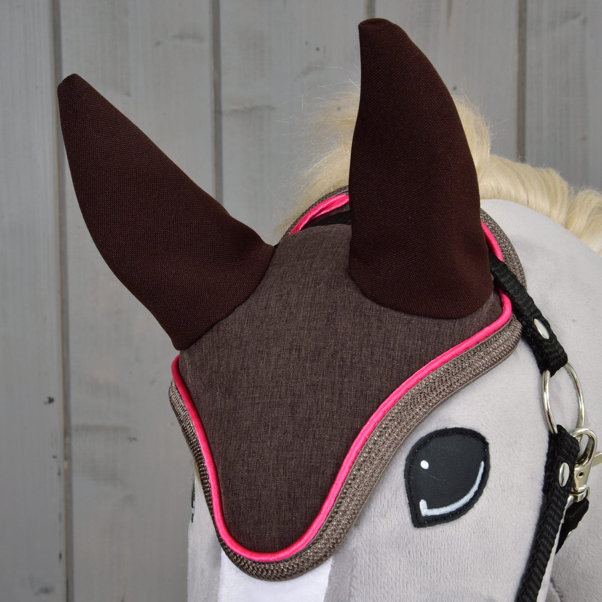 Close-up of brown ear bonnet with bright pink edging on a grey Hobby Horse