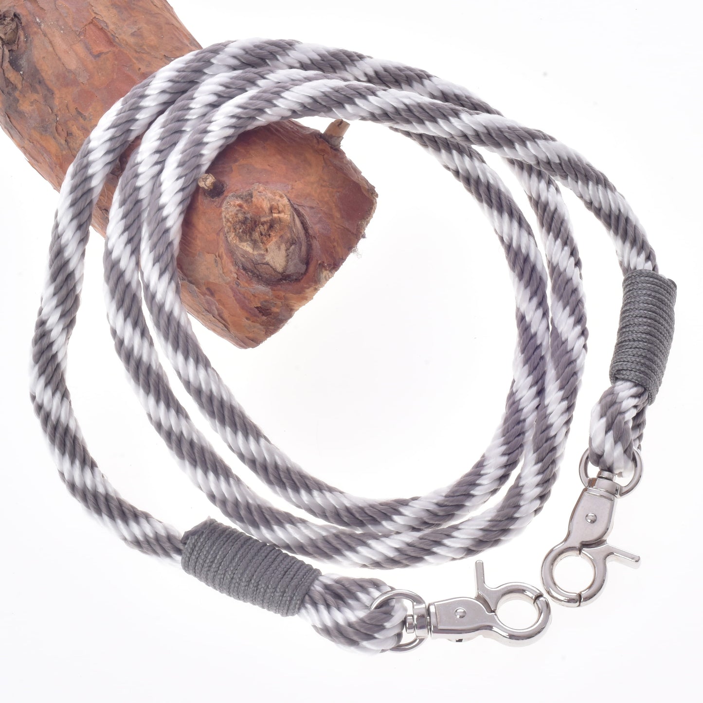 The Set Start Silver by Hobby Horse LarDen—a black, white, and gray twisted rope included as reins or a halter and lead rope—features metal clasps on each end and is coiled around a piece of brown wood, shown against a white background.