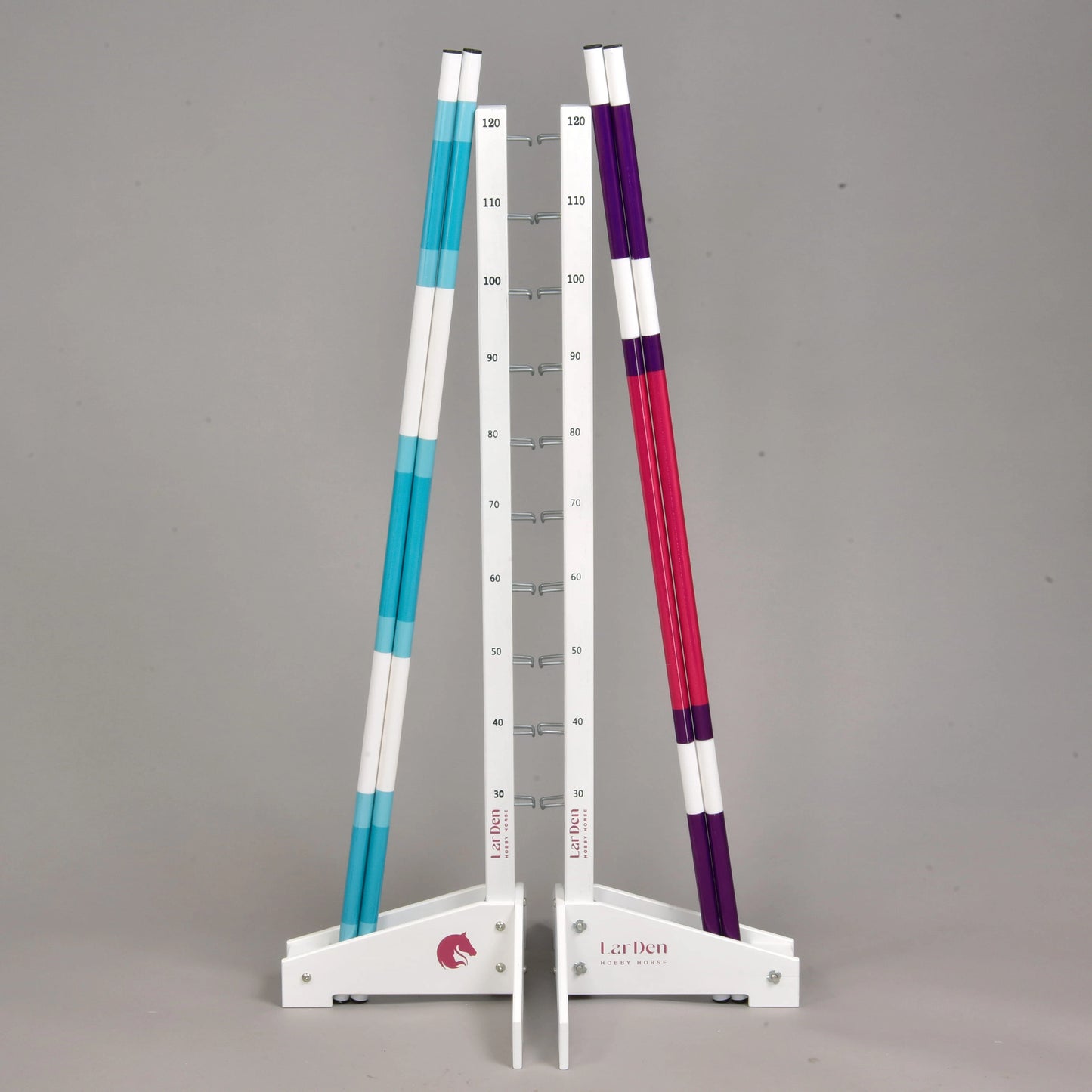 The Jump 120 cm / 47 inch with Extra Poles by Hobby Horse LarDen features two white stands with measurement markings holding three striped poles—two blue, one purple. This adjustable obstacle suits indoor or outdoor Hobby Horsing practice on a gray background.
