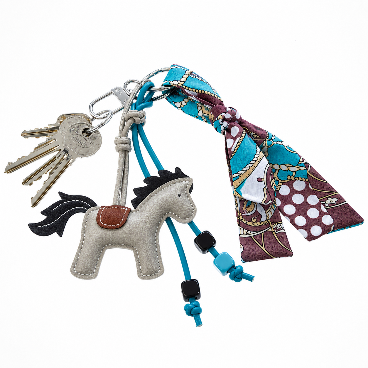 A set of keys on a ring with the Hobby Horse LarDen Keychain Horse Grey, blue beaded cords, and a colorful blue, brown, and white patterned scarf tied to the keyring.