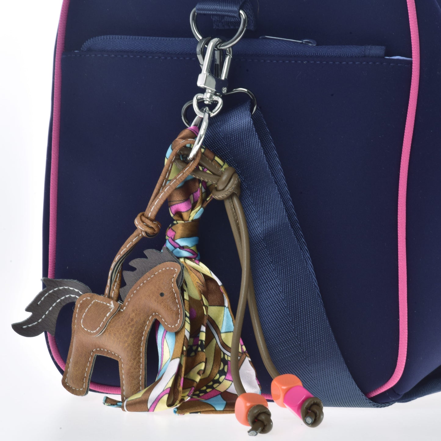 The Hobby Horse LarDen Keychain Horse Brown—adorned with a colorful scarf, orange and pink beads—accessorizes your navy blue bag with pink trim and blue strap, making it perfect for hobby horsing fans.