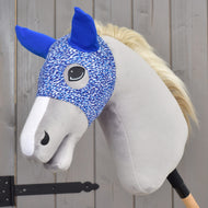 A Hobby Horse LarDen "Horse Mask See" plush hobby horse, featuring a blue and white washable PES mask, blue ears, a light gray face, and a white mane, is attached to a stick and placed in front of a wooden fence.