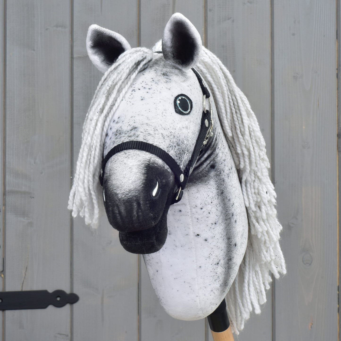 A gray Hobby Horse LarDen "Naivy" with a white yarn mane, black halter, and button eyes (size S), is positioned in front of a wooden fence.