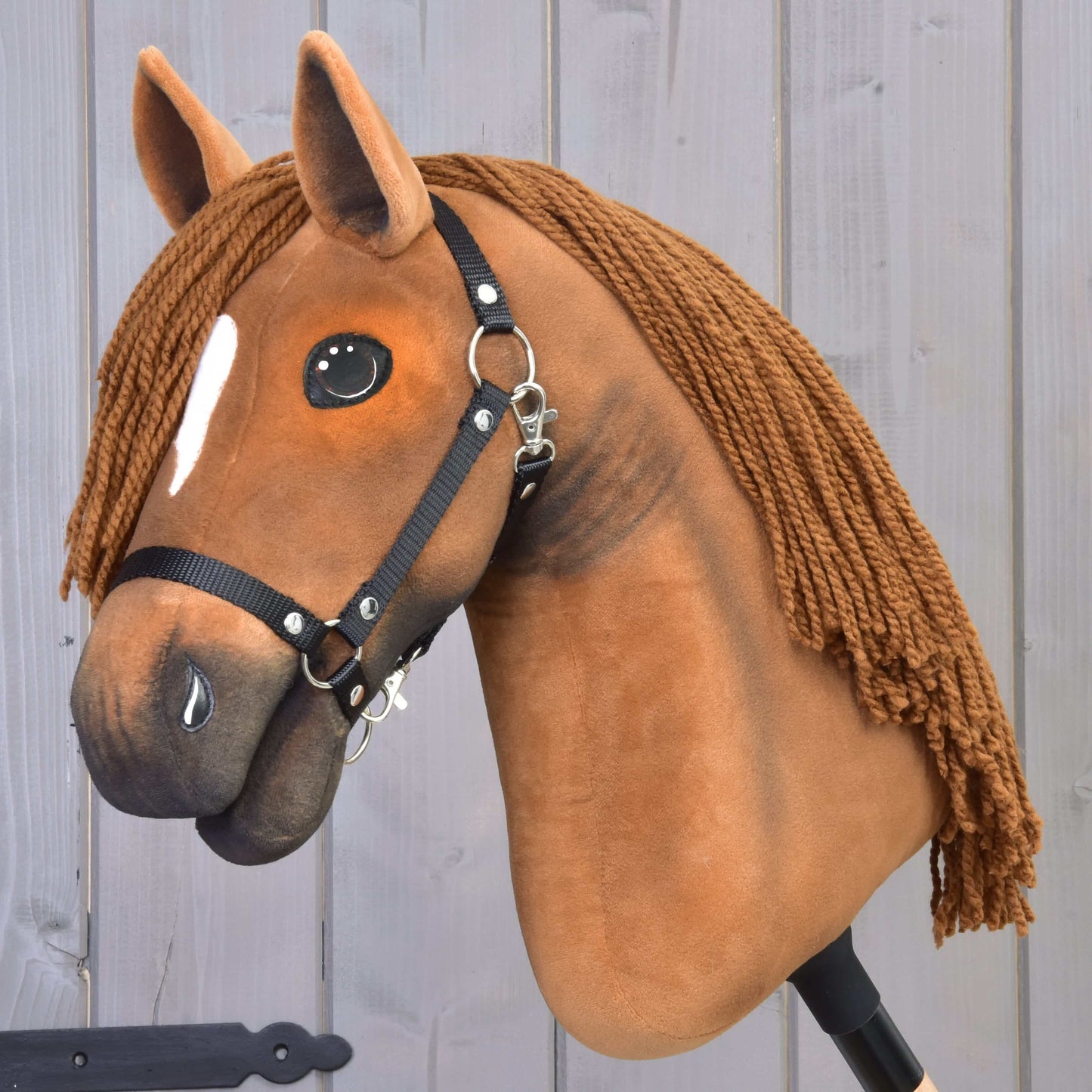Hobby Horse Pippa with Black Halter showing detailed face, brown yarn mane, and soft plush material against wooden background