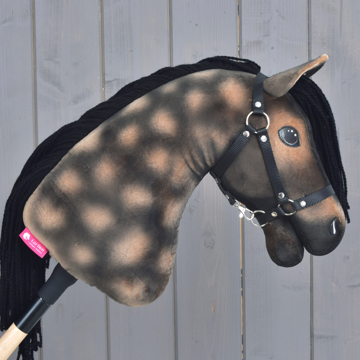 The Hobby Horse LarDen “Hobby Horse Stormy with Black Halter” showcases a dappled brown and black plush head inspired by a Hanoverian stallion, complete with a black yarn mane and black halter, set against a light wooden background.