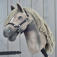 The Hobby Horse LarDen "Hobby Horse Swing with black halter," size S, features a plush horse with a braided yarn mane and a sleek black halter, mounted on a stick and showcased against a wooden backdrop.
