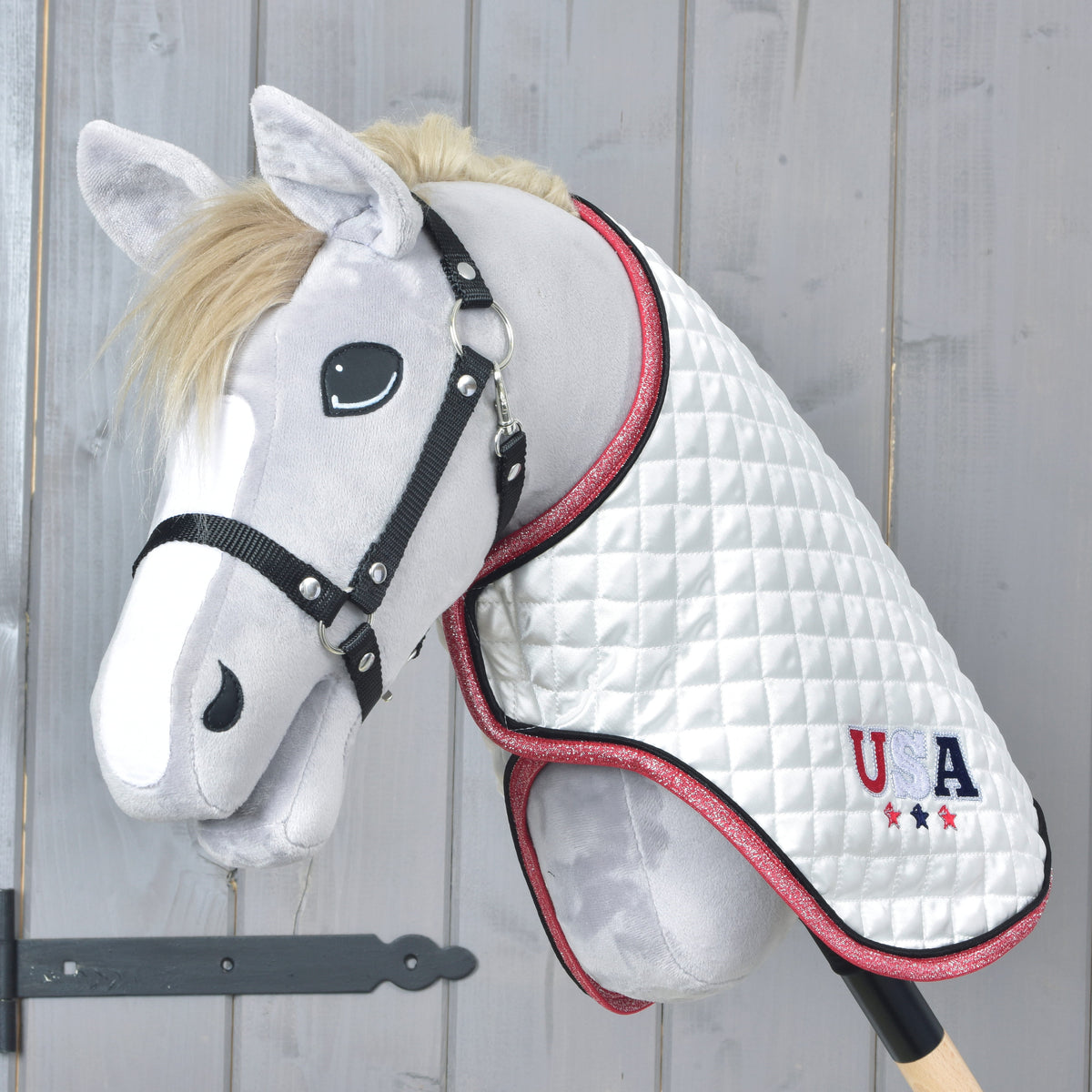 Grey Hobby Horse with black halter wearing a white quilted blanket with USA embroidery and sparkly pink edging