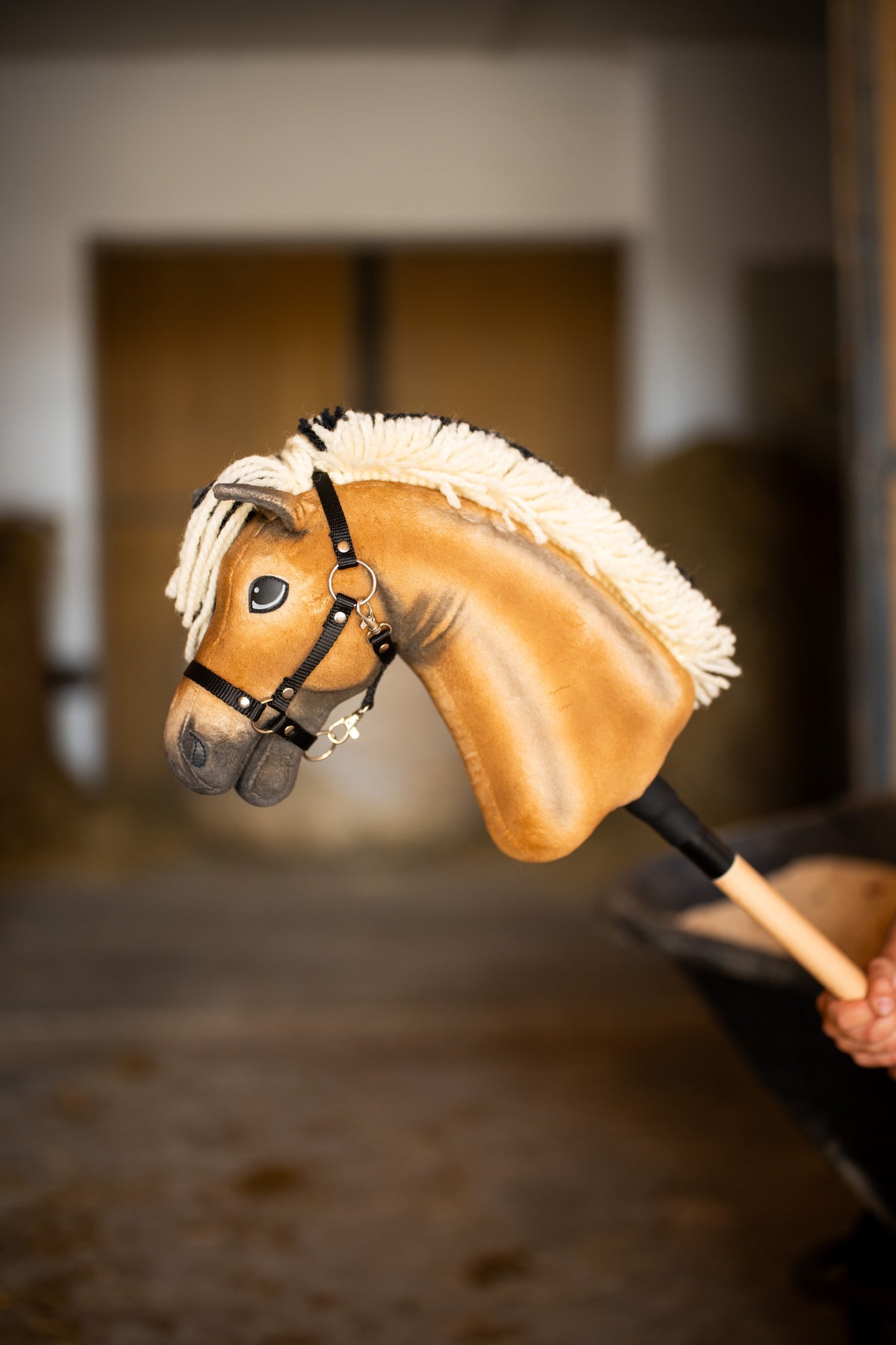 Detail photo: the head of the Hobby Horse Colby with black Halter by Hobby Horse LarDen held up in a stable, the stalls blurred behind - palomino plush, cream yarn mane and forelock, black halter.