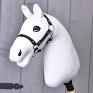 A “Build your horse” white plush hobby horse head—featuring a black bridle and mounted on a stick—is displayed against a light gray wooden background, offering an inviting way to customize your own one-of-a-kind creation.
