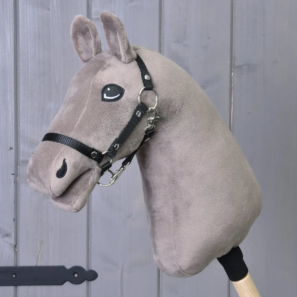 The Build your horse, by related_to_12441055625556, is a taupe hobby horse with a plush head, black yarn mane, bridle and reins on a wooden stick, shown against gray wood panels.