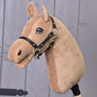A "Build your horse" plush toy by related_to_12441055625556, featuring caramel-colored light brown fur, a cappuccino mane, a black bridle, and a friendly embroidered eye, posed in front of a gray wooden wall.